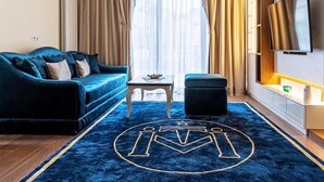 Moderni hotellihuone, jossa on sininen sohva, pieni pöytä, televisio ja suuri ikkuna, jossa on verhot.