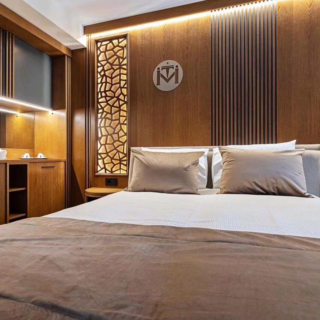 A hotel room with a bed, a nightstand, a wooden wardrobe, and a decorative wall panel.