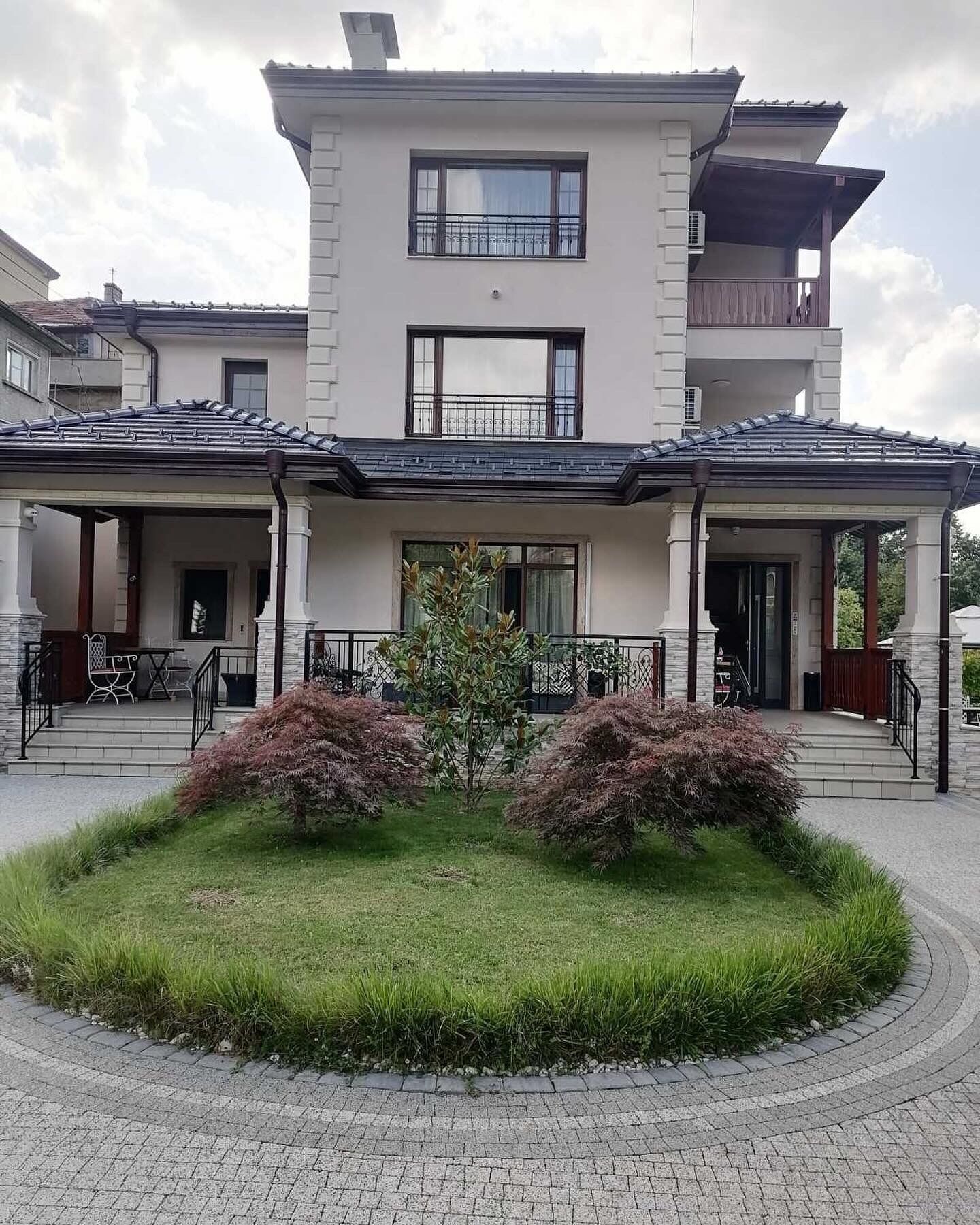 Una casa moderna de dos pisos con un porche cubierto, un pequeño jardín y un camino de entrada pavimentado.