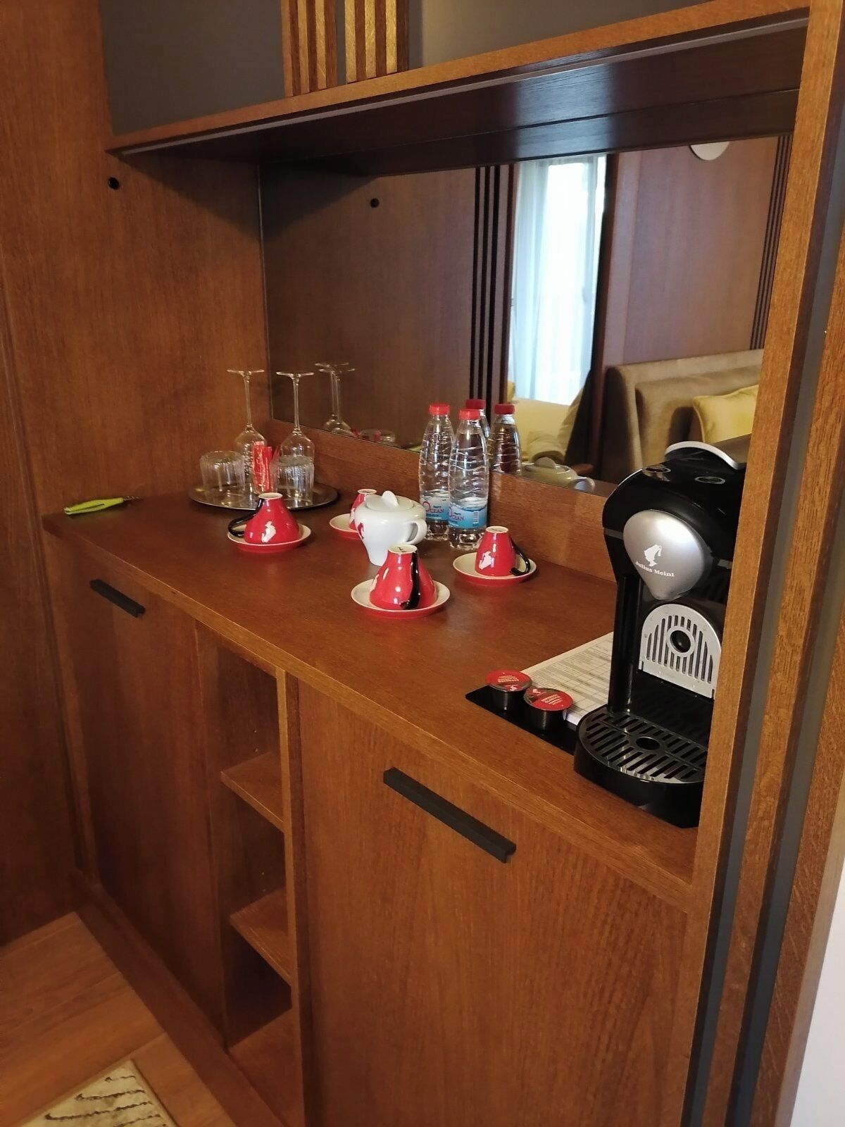 Una kitchenette compacta con cafetera, botellas de agua y un portavasos para copas de vino.