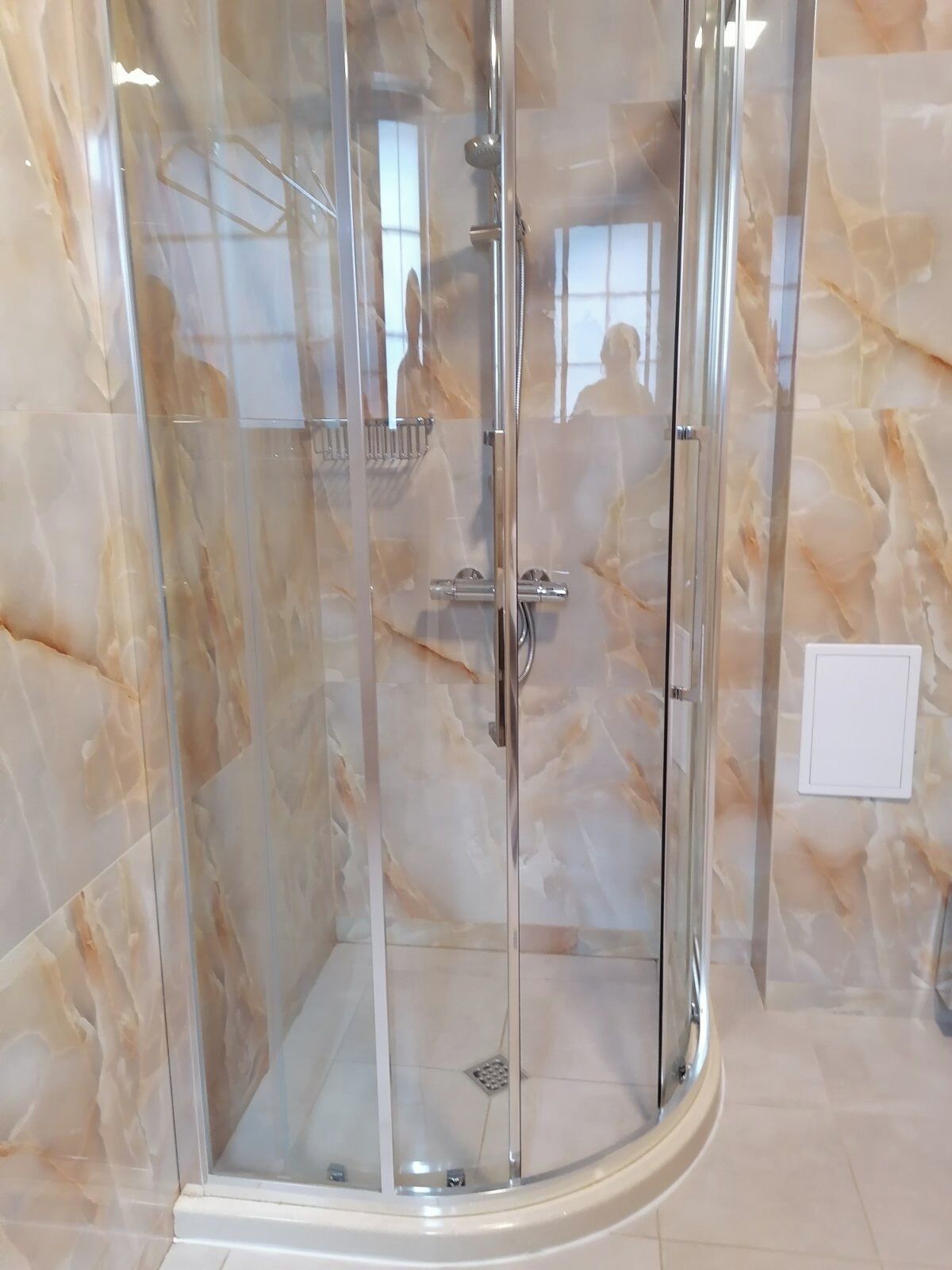 A glass-enclosed shower with a marble wall, a control panel, and a visible drain.