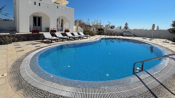 A swimming pool with lounge chairs, a white building with arched doorways, and a clear blue sky. - Villa Galathea (Episkopi Gonias)