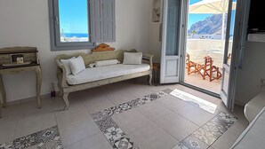 A room with a sofa, a small table, a window with shutters, and a door leading to an outdoor area with a table and chairs. - Villa Galathea (Episkopi Gonias)