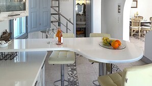 A modern kitchen with a central island, bar stools, a chandelier, and a staircase leading to an upper level. - Villa Galathea (Episkopi Gonias)