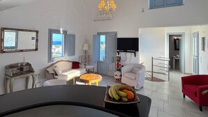 A spacious living area with a large window, a chandelier, and a fruit bowl on a table. - Villa Galathea (Episkopi Gonias)