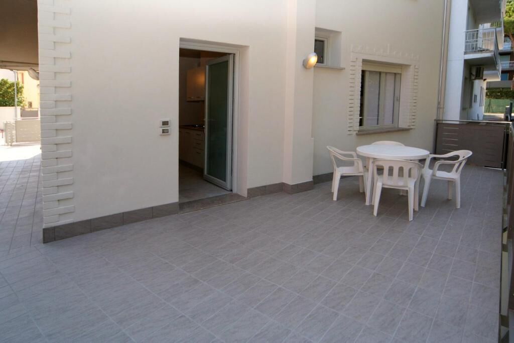 A patio with a table and chairs, a door leading to an interior space, and a small window with shutters.