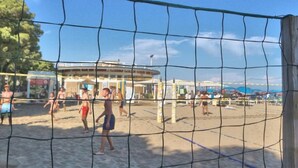 A beach volleyball court with a net, sand, and a building in the background. - Renovated Residence Just Steps From the Beach (Lignano Sabbiadoro)