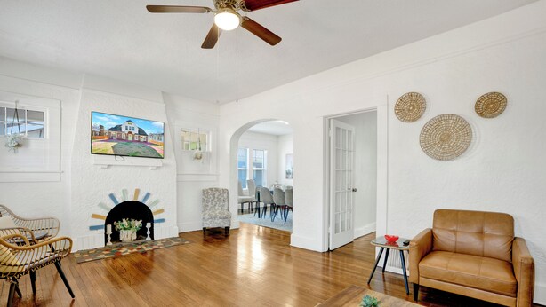 A spacious living room with hardwood flooring, a fireplace, a ceiling fan, and a large TV mounted on the wall. - Spacious 6-bedroom apartment in gorgeous Birmingham with AC, secured parking lot (Birmingham)