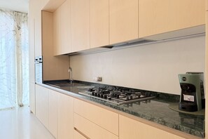 Une cuisine équipée d’une cuisinière à gaz, d’une machine à café et de meubles de rangement en bois clair.