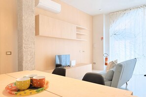 Un salon moderne comprenant un canapé, une table à manger avec un panier de fruits, un téléviseur à écran plat et des étagères intégrées.