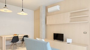 A modern living room with a sofa, a dining table with chairs, a TV, and built-in shelves. - P085 – Porto Recanati, new two-room apartment 30 meters from the sea (Porto Recanati)