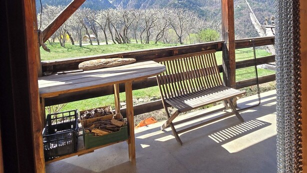 Un banc et une table en bois, placés sous un toit en tôle ondulée, avec vue sur la montagne.
