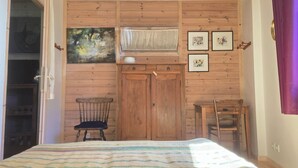 Une chambre avec des murs recouverts de lambris en bois, un lit avec une couverture à rayures, une chaise, une armoire et des tableaux encadrés.