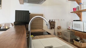 Une cuisine dotée d’un plan de travail en bois, d’un évier en acier inoxydable, d’un four à micro-ondes et d’une étagère en bois où sont rangés des bocaux.