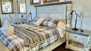 Een slaapkamer met een groot bed, twee nachtkastjes, een kaptafel en een raam met uitzicht op bomen.