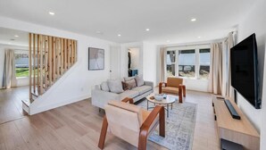 Uma sala de estar moderna com um sofá, poltronas, uma mesa de centro, uma televisão e uma escada com guarda-corpos de madeira.