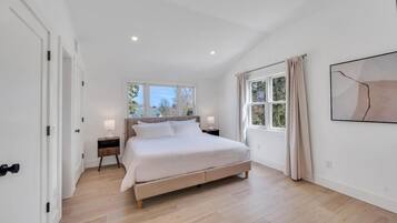 Ein Schlafzimmer mit einem Bett, Nachttischen, einem Fenster mit Vorhängen und einem Bild an der Wand.