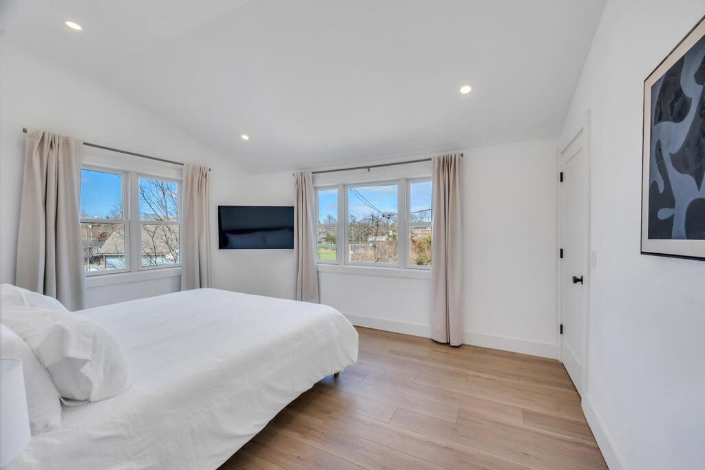 A bedroom with a bed, two windows, a mounted TV, and a door.