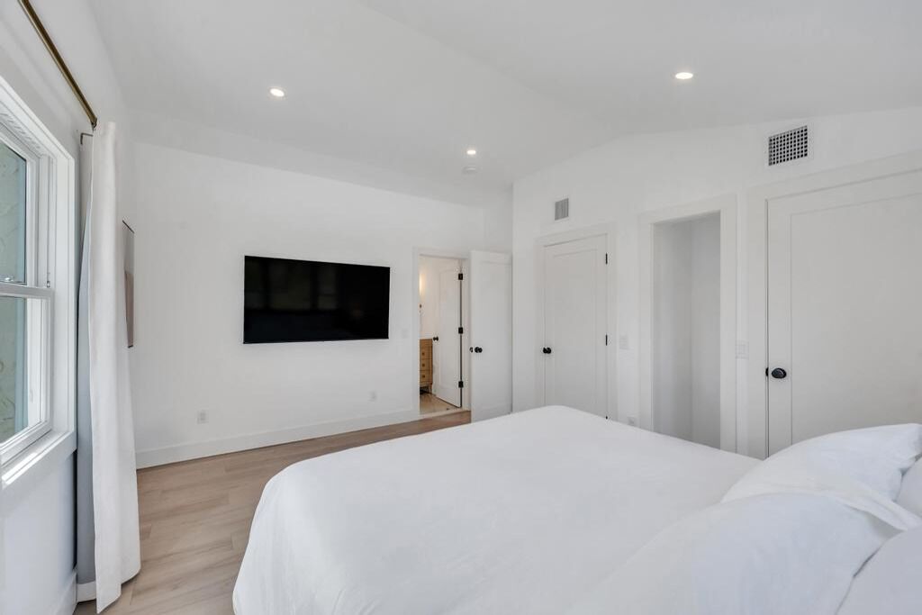 A bedroom with a large bed, a TV mounted on the wall, and a door leading to another room.