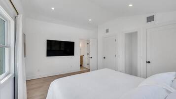 A bedroom with a large bed, a TV mounted on the wall, and a door leading to another room.