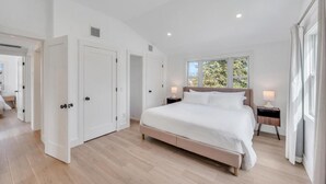 Quarto com uma cama grande, uma mesa de cabeceira, uma janela com vista e uma porta que dá para outro espaço.