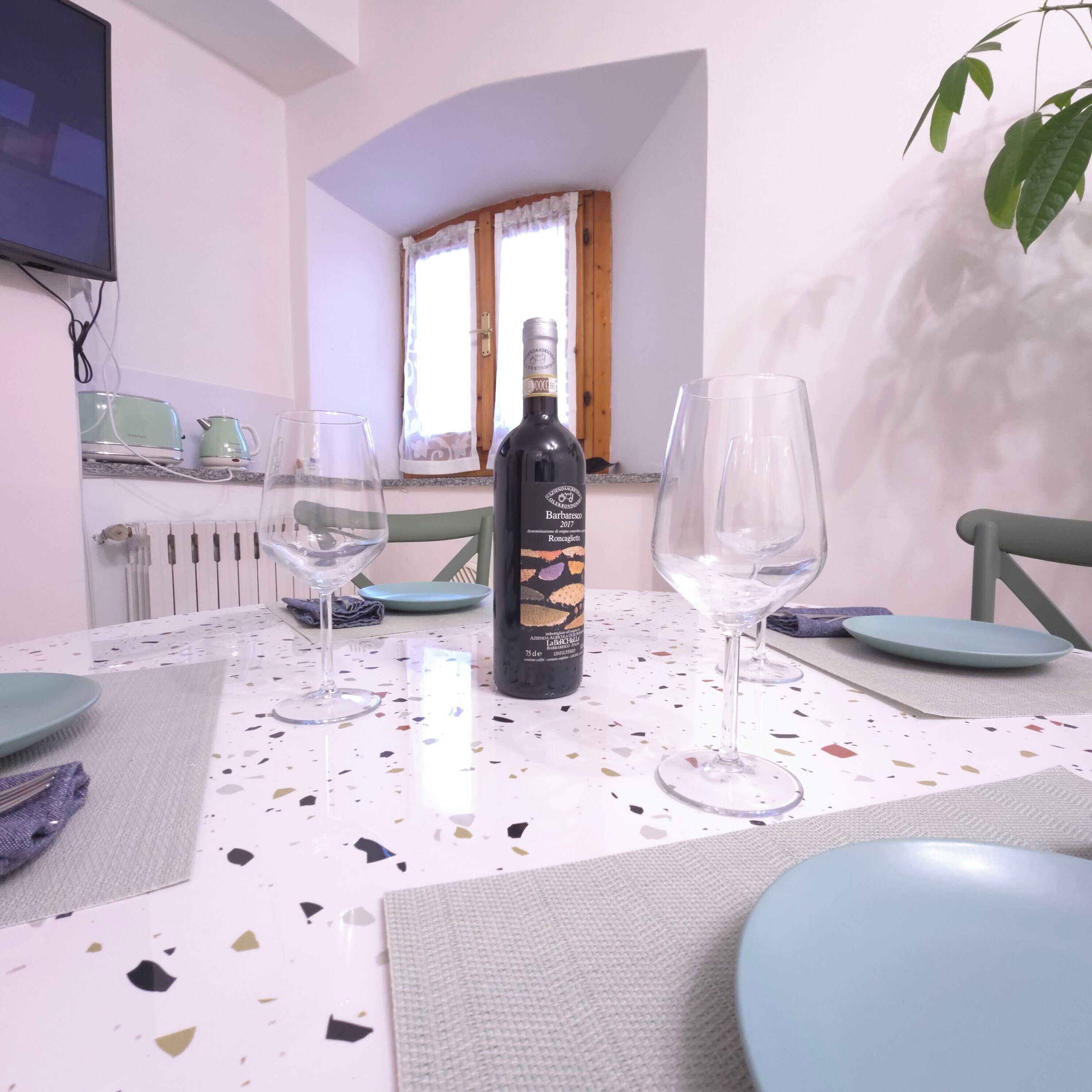 A dining table with a wine bottle, two glasses, and plates, in a room with a window and a radiator.