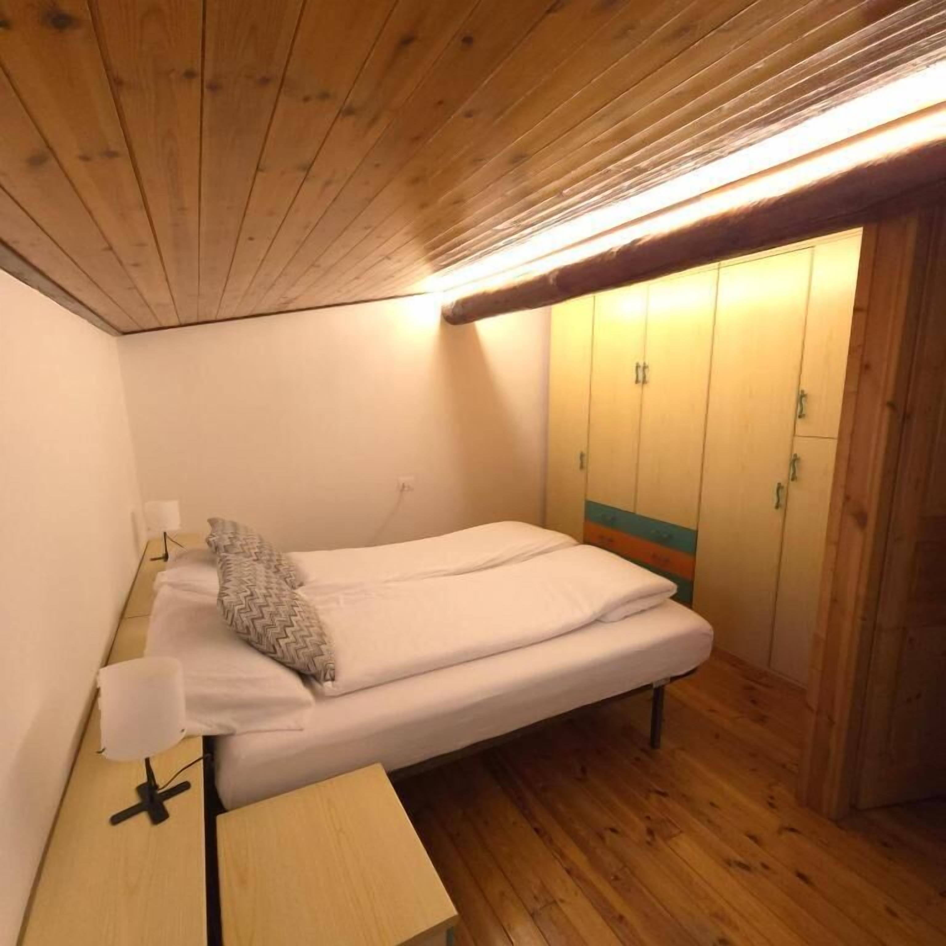 A small, single-bed room with wooden flooring, a bedside table, and a wardrobe with a teal accent.