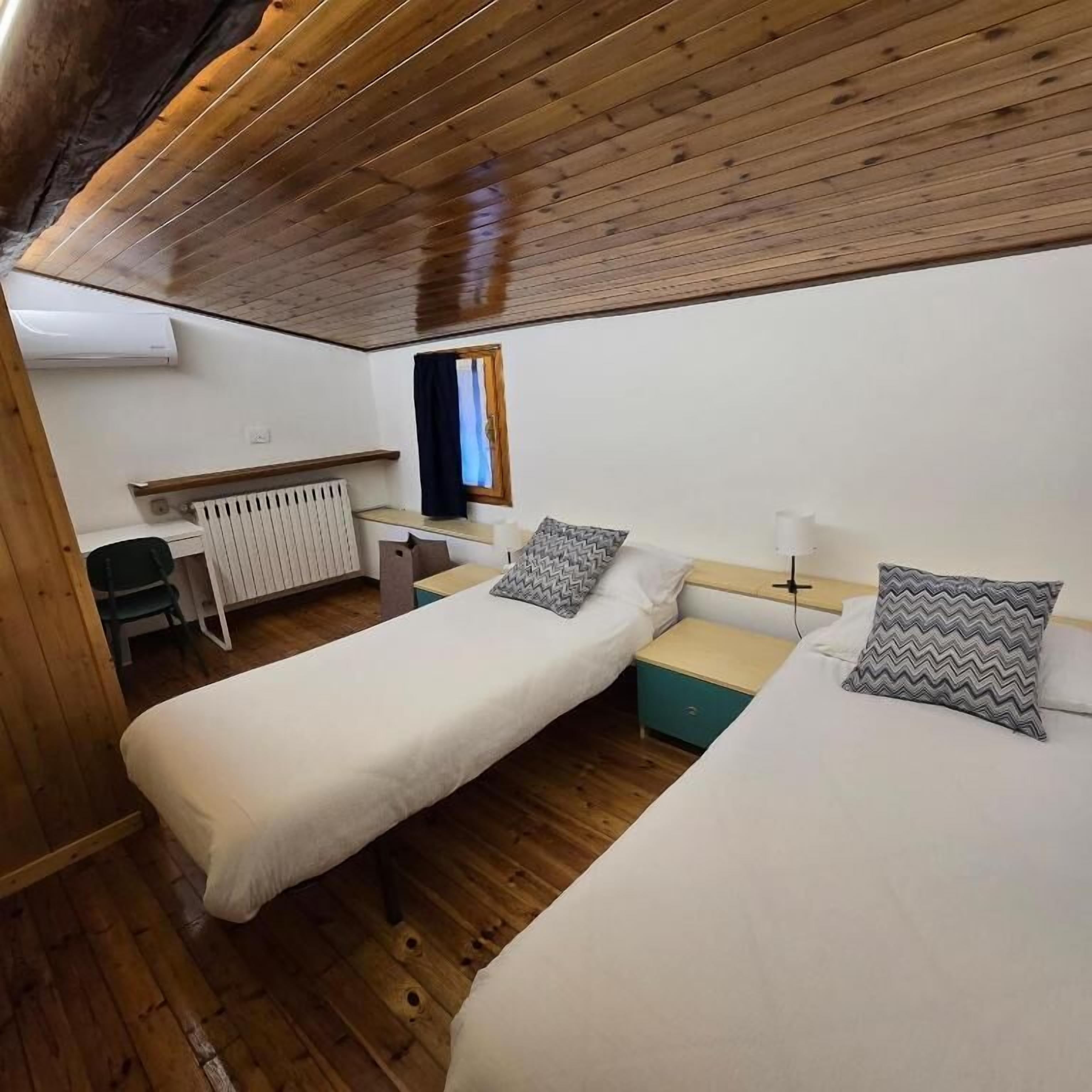 Une chambre avec deux lits, un bureau, une chaise et une fenêtre.