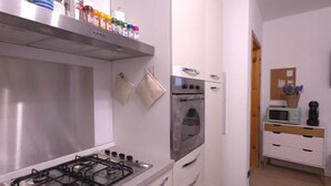 A modern kitchen with a gas stove, oven, and microwave. There are cabinets and a shelf with jars and containers. - Orio welcome BGY (Bergamo)