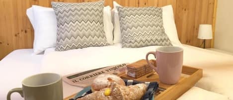 A bed with wooden headboard, pillows, a tray with a mug, a plate with pastries, and a newspaper.