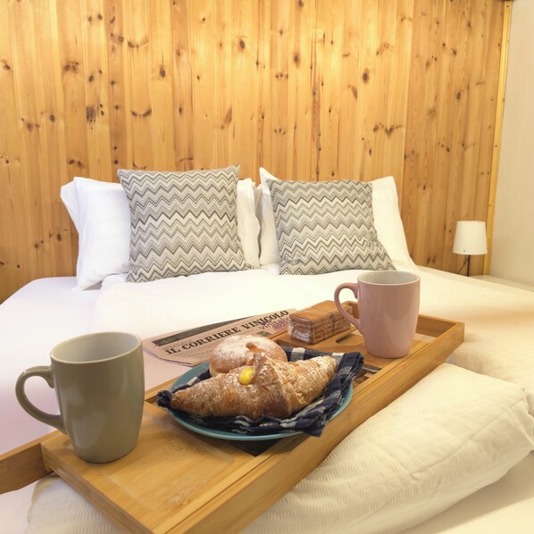 A neatly made bed with a wooden headboard, a tray with pastries and a mug, and a lamp in the corner. - Orio welcome BGY (Bergamo)