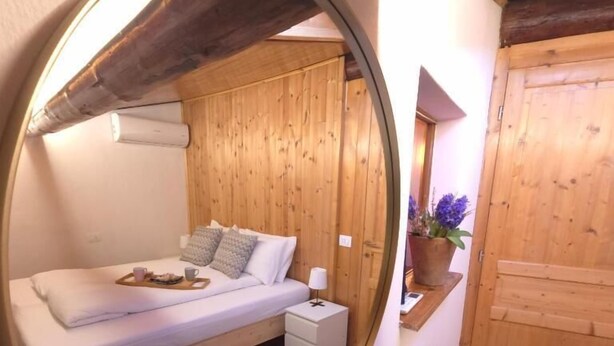 A bedroom with a bed, bedside table, lamp, and a mirror reflecting the room. - Orio welcome BGY (Bergamo)