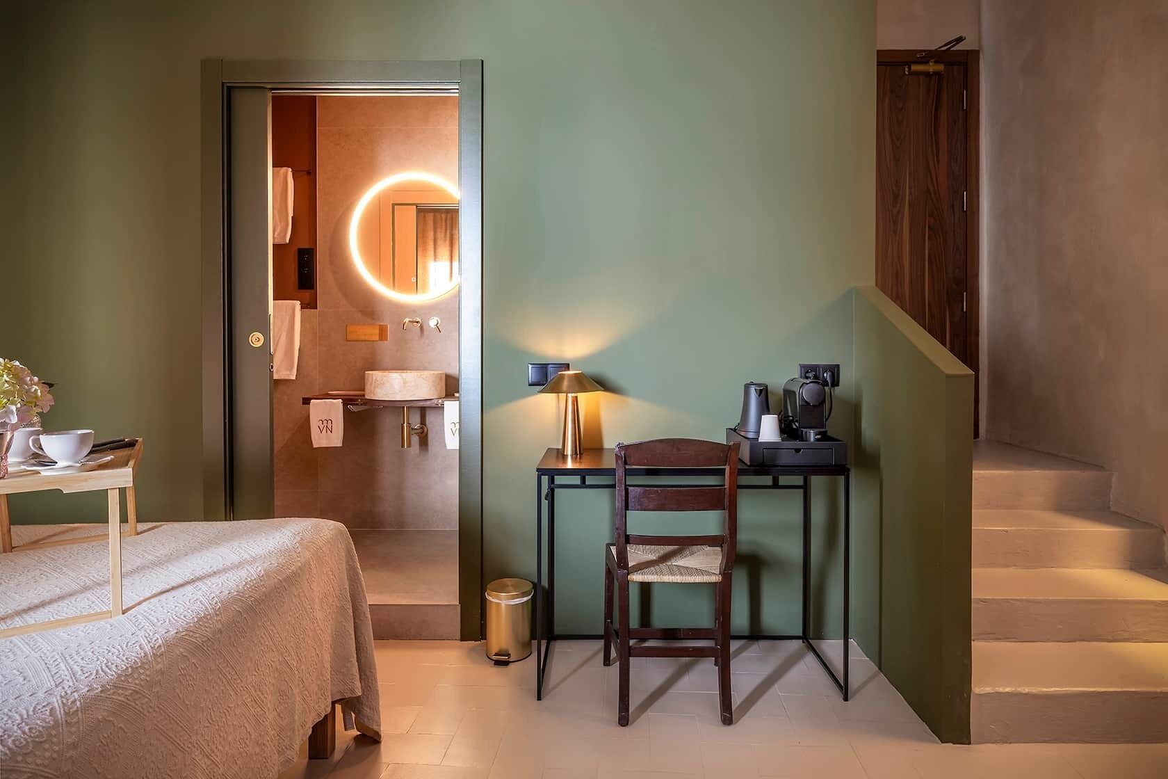 Habitación de hotel con cama, escritorio, silla, cafetera y cubo de basura.
