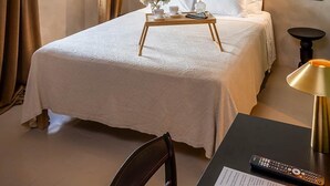 Une chambre d’hôtel comprenant un lit, un ventilateur de plafond, une fenêtre avec des rideaux, une table de chevet avec un plateau et une lampe.
