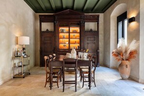Un coin repas avec une table en bois, des chaises, une bibliothèque et un vase contenant des plumes d’herbe des pampas.