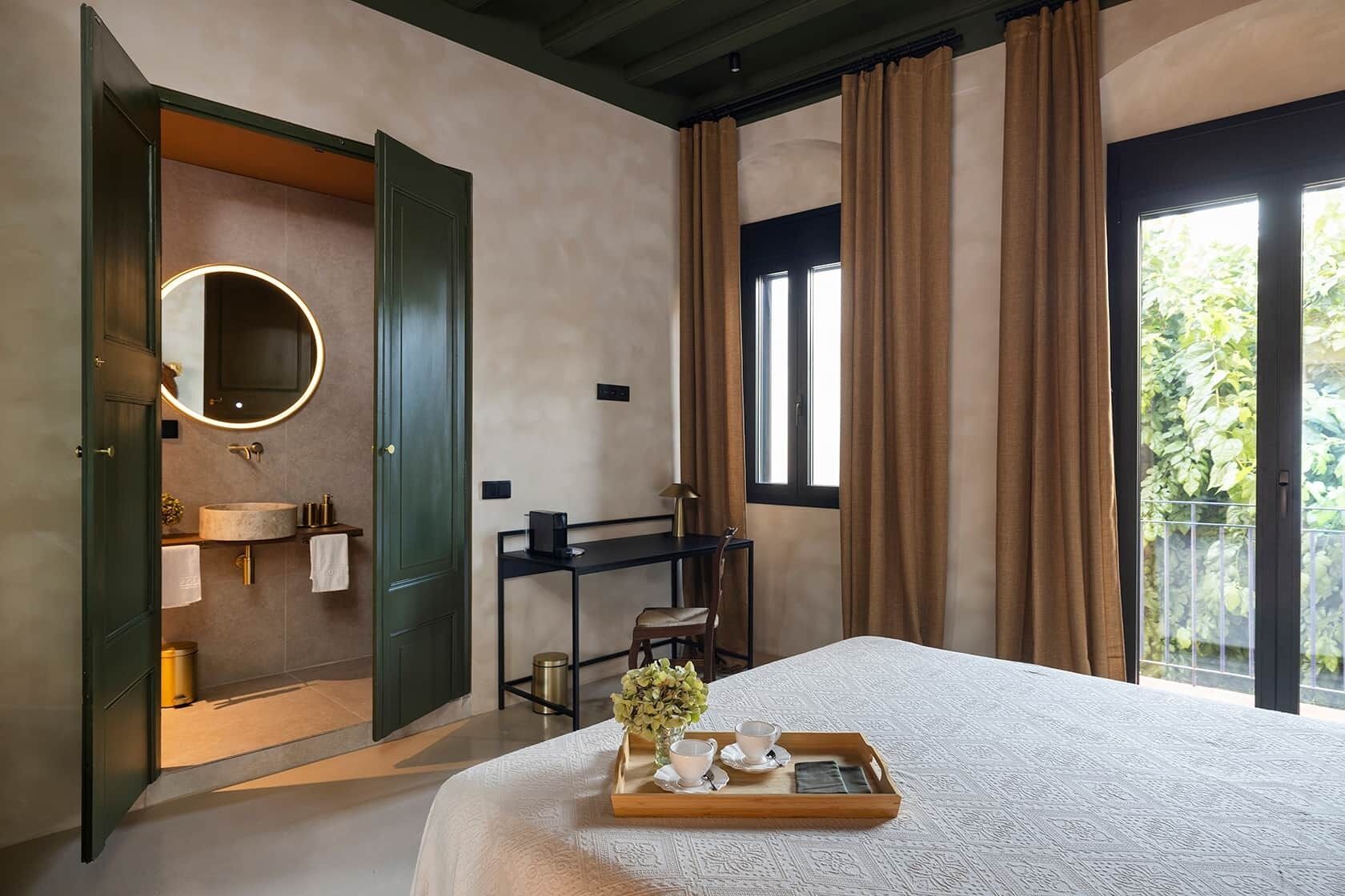 Une chambre d’hôtel avec un lit, une salle de bain avec un miroir, un bureau et une vue sur la verdure.