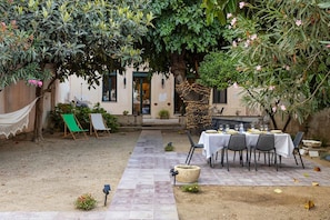 An outdoor dining area with a table set for four, surrounded by greenery and a hammock.