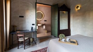 A bedroom with a bed, a desk, a chair, a mirror, and a bedside table with cups.