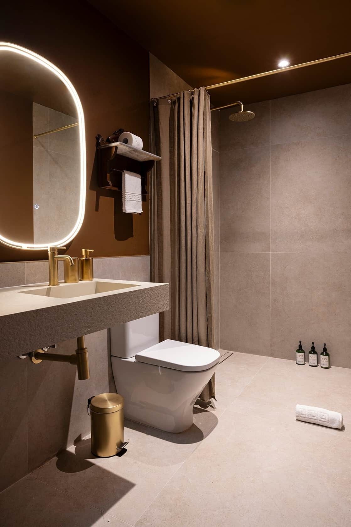 Un baño moderno con un espejo redondo, detalles dorados, un inodoro y una ducha.