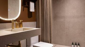 Un baño moderno con un espejo redondo, detalles dorados, un inodoro y una ducha.