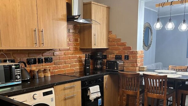 Una cocina con armarios de madera, lavavajillas, estufa y un comedor con sillas y una mesa.