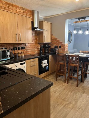 A kitchen with wooden cabinets, a dishwasher, a stove, and a dining area with chairs and a table.