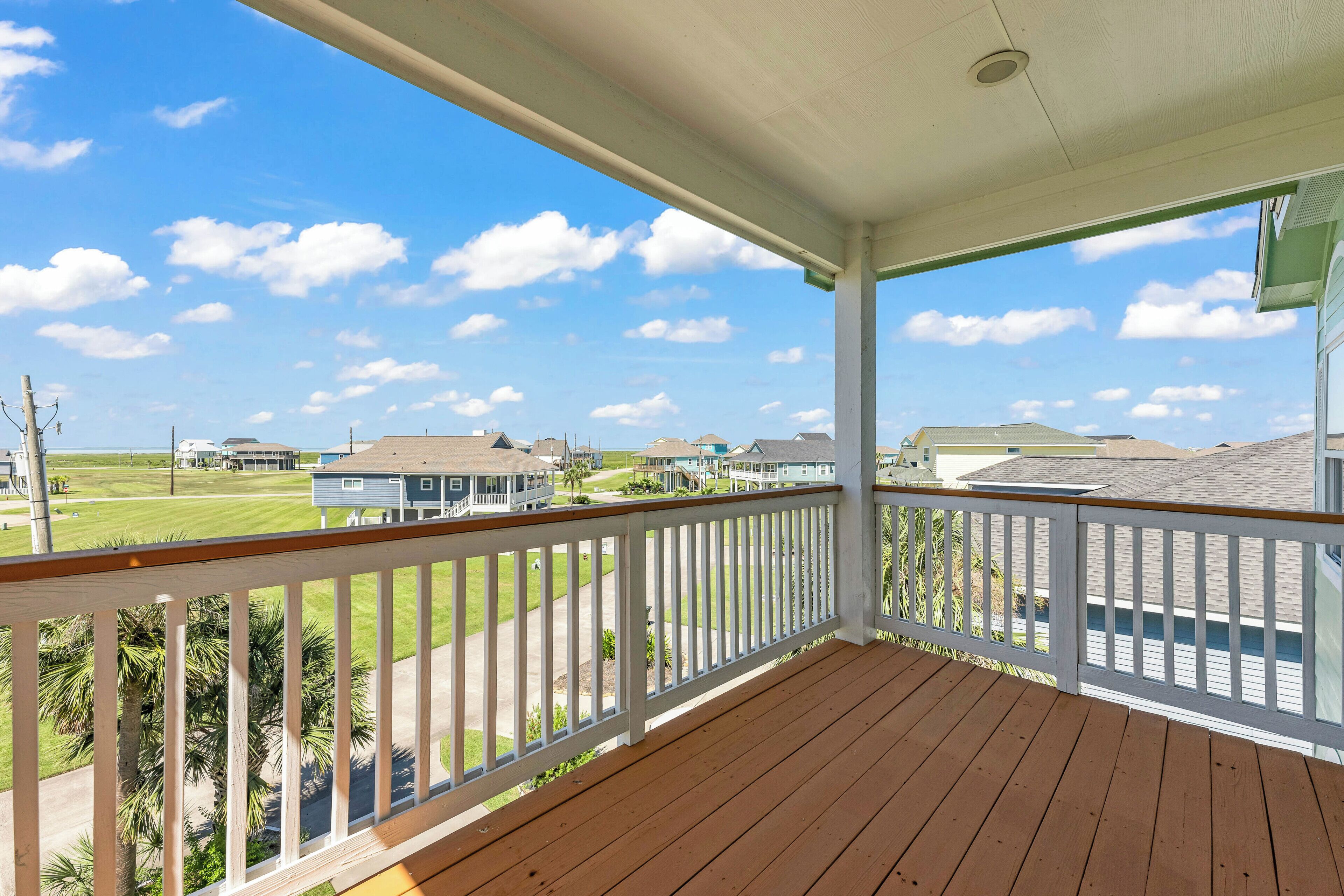 A wooden deck with a white railing, overlooking a residential area with houses and a golf course.