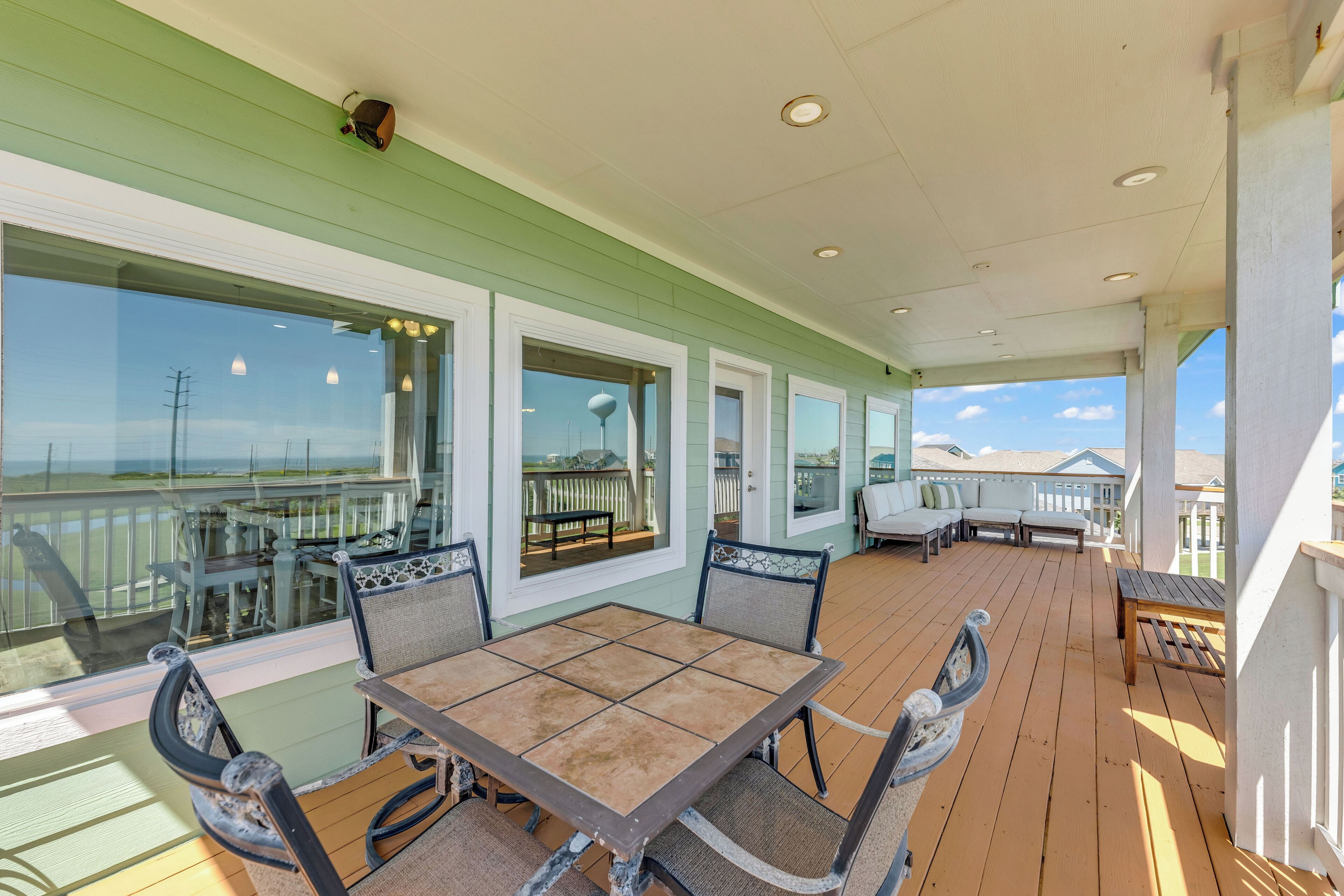 A covered outdoor area with a wooden deck, a table with four chairs, and a view of the ocean through large windows.