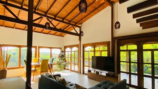A spacious living area with a high ceiling, large windows, a sofa, a TV, and a dining area. - Private Countryside Retreat Jacuzzi & Scenic View (pereira)