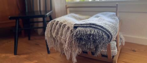 Pieni puinen sänky, jossa on peitto, tuoli ja ikkuna, josta avautuu näkymä vehreään maisemaan.