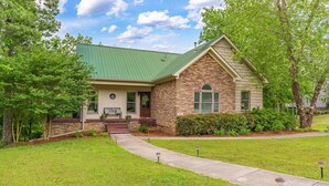 A two-story stone building with a green roof, a front porch, and a pathway leading to the entrance. - Spacious 5 bedroom house with double decker dock on quiet lakefront! (Arley)