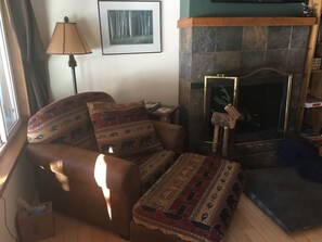 Een woonkamer met een bank, poef en een open haard.
