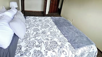 Een slaapkamer met een bed, nachtkastje, lamp, kledingkast en een deur naar een andere kamer.