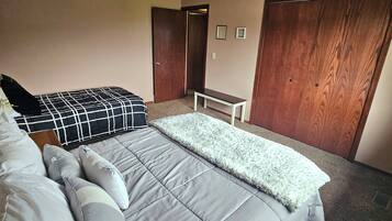 Un dormitorio con una cama, almohadas, una mesita de noche, un armario de madera y una lámpara en el techo.